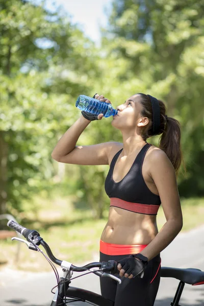 Prześcignąć kobieta lekkoatletycznego wody pitnej po korzystanie z rowerów, — Zdjęcie stockowe