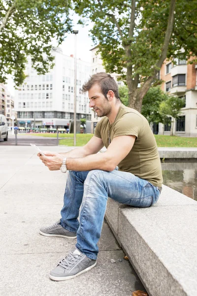 Casual adam sokakta oturan ve tablet bilgisayar holding. — Stok fotoğraf