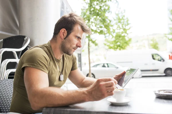 Man zit in de terrasbar met koffie beker en laptop, tablet pc. — Stockfoto