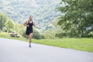 Parkta koşan atletik adam gülümseyen.