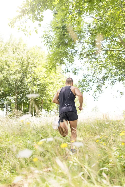 Atletisk man kör ner fältet en solig dag. — Stockfoto