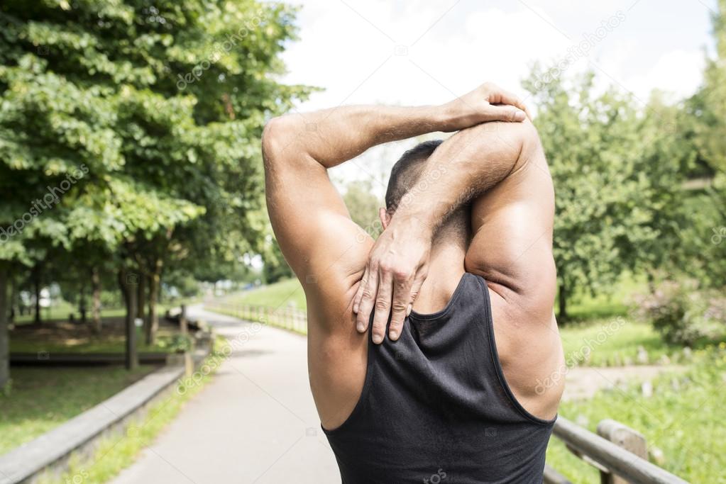Closeup of back athletic man doing stretches before exercising, outdoor.
