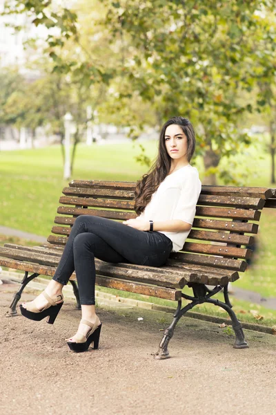 Elegante mooie vrouw zittend op een bankje in het park. — Stockfoto