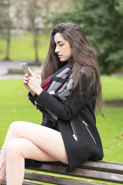 Hermosa mujer joven elegante utilizando el teléfono inteligente en el parque . — Foto de Stock