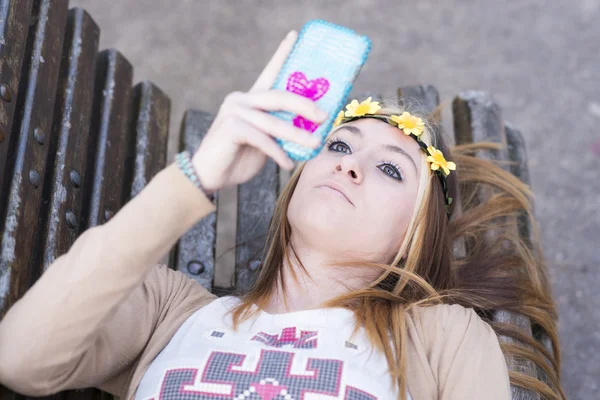 Felicidade menina bonita com telefone inteligente deitado no banco . — Fotografia de Stock