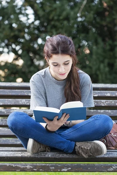 Smiling young woman sitting on bench and reading book, outdoor. — Stock Photo, Image