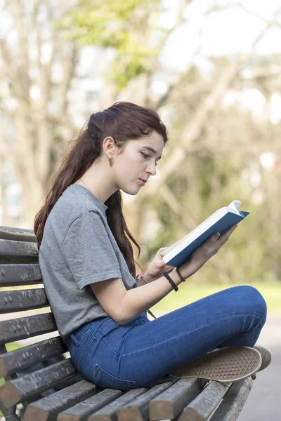 Hermosa chica caucásica sentada en el banco, leyendo libro azul . — Foto de Stock