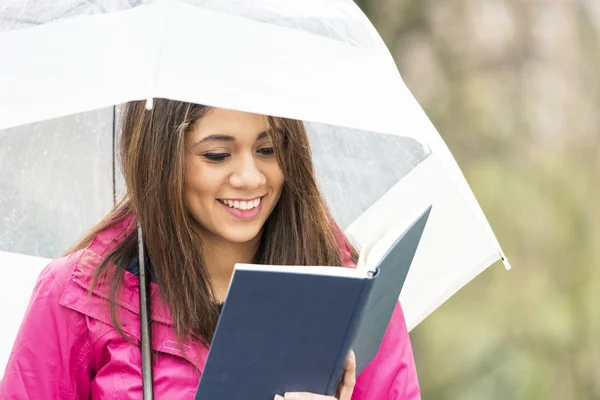 微笑的女人用的伞在公园里看书. — 图库照片