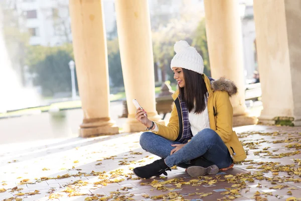 Mooie glimlachend womanwith telefoon zittend op Bladeren. — Stockfoto