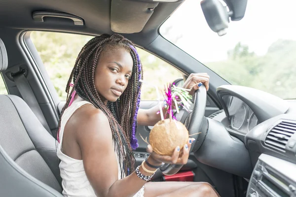 Mooie Afrikaanse vrouw met kokos cocktail in de auto. — Stockfoto