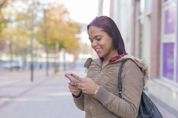 通りでスマート フォンを持つ若い女性を笑顔. — ストック写真