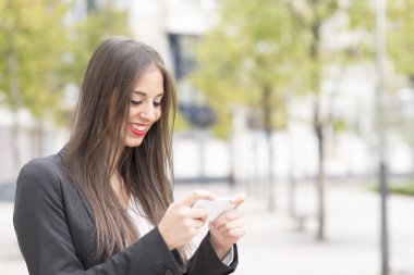 Akıllı telefon kullanan sokağın ortasında gülümseyen iş kadın.