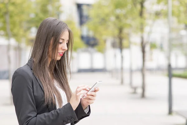 Uśmiechnięta kobieta biznesu przy użyciu inteligentnych telefonów na ulicy. — Zdjęcie stockowe