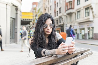 Bankta oturan ve sokakta akıllı telefon kullanan kadın.