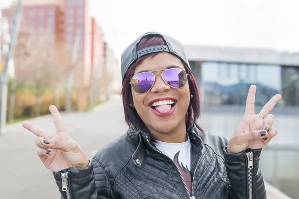 Hipster begeistert schöne Frau mit Sonnenbrille zeigt ihre Zunge auf der Straße. — Stockfoto