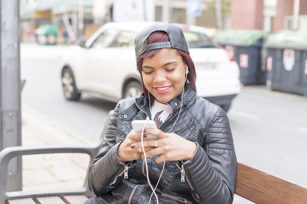 Donna sorridente seduta sulla panchina e ascoltare andare musica, concetto di stile di vita urbano . — Foto Stock