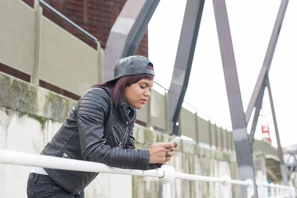 Mulher de moda com boné de beisebol olhando mensagem seu telefone inteligente na rua . — Fotografia de Stock