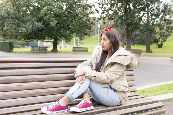 Jeune femme réfléchie assise sur un banc et regardant ailleurs . — Photo