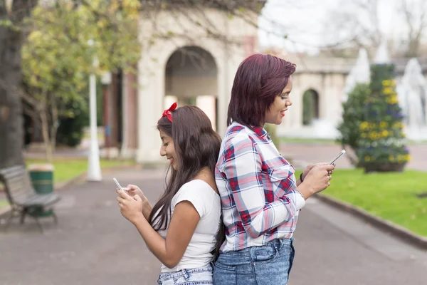 Deux amies souriantes partageant les médias sociaux dans un téléphone intelligent . — Photo