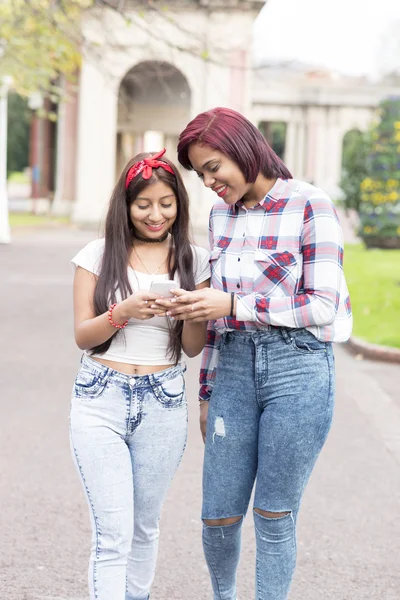 Dos amigas sonrientes compartiendo redes sociales en un teléfono inteligente . Imagen de archivo