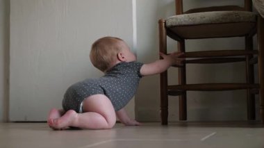 Adorable infant enthusiastically holds onto a chair, demonstrating his growing independence and developing motor skills in a warm and cozy home environment