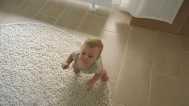 Yuvarlak halıda sürünen bebek, yumuşak güneş ışığı, yumuşak gölgeler, tepedeki kamera açısı meraklı bir bebeğin fayans zeminini, elleri ve dizlerini keşfetmesini, rahat ev ortamını görüntüler.