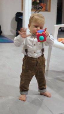 Pantolon askılı bir bebek oyuncağı inceler, küçük bir çocuk çevreyi keşfeder, bebek sıcak fayans zeminde ilk adımlarını atar.