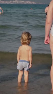 Deniz kıyısındaki çocuklar, sakin dalgaları keşfeden küçük bir çocuk, kumlu sahil şeridinde oynayan çocuklar, platin saçlı küçük bir çocuk, güzel havalarda sığ suların tadını çıkaran sığ bir çocuk.