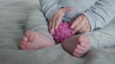 Renkli oyuncaklarla hareket becerileri geliştiren bebek, yumuşak battaniyede top tutuşu ile dokunsal dokuları keşfeden bebek, motor beceriler ve dokunsal farkındalık geliştirmek için duyusal nesnelerle uğraşan çocuk.