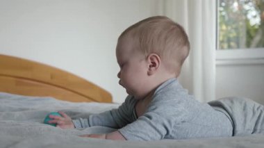 Bebek oyuncakları inceliyor, çocuk yatakta dikkatlice çalışıyor, küçük çocuk yumuşak renkli topları inceliyor, bebek rahat yatakta uzanıyor, parlak renkli küresel oyuncaklara merakla uzanıyor.