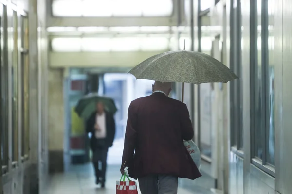 Senior adults with umbrellas in passage — Stock Photo, Image