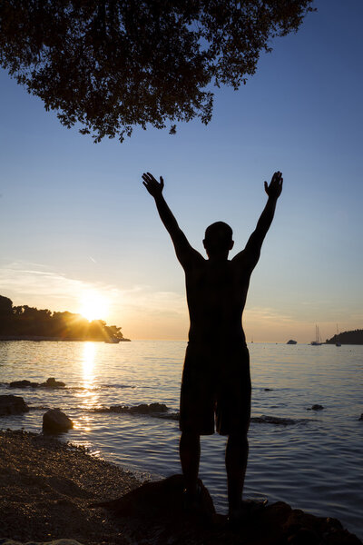 Man saluting sun on shore