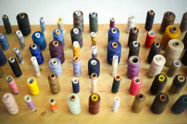 Sewing threads displayed on wooden board — Stock Photo, Image