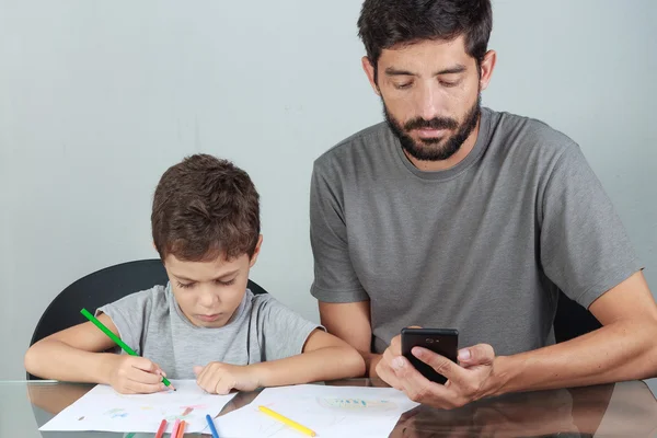 Father using smartphone while your child draws with colored penc — Stock Photo, Image