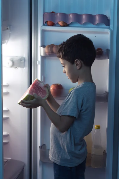 Child looking at a watermelon in front of the refrigerator in th — Stock Photo, Image