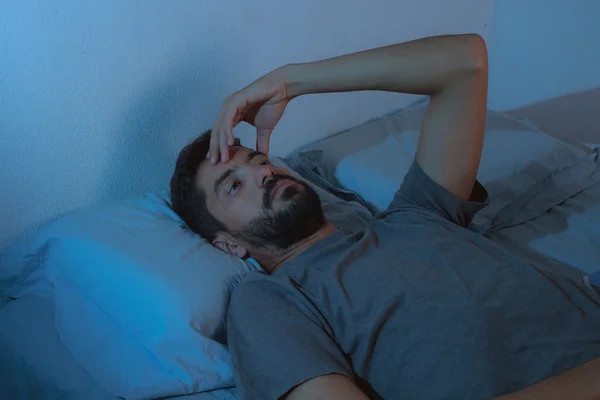 Poruchy spánku, nespavost. mladá vousy muž ležící na posteli vzhůru — Stock fotografie