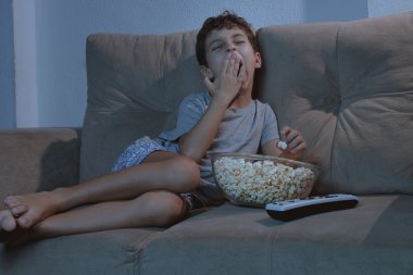 Küçük çocuk Tv izlerken, yemek popc kanepede esneme