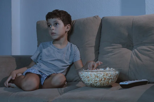 Kleiner Junge auf der Couch fernsehen und essen Popcorn in der Nacht i — Stockfoto