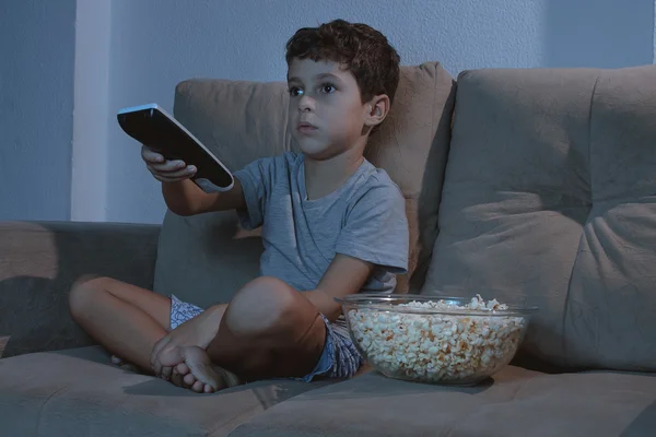 Small boy on the couch watching TV and eating popcorn at night i — Stock Photo, Image