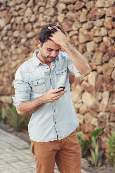 Utomhus porträtt av orolig ung man med mobiltelefon i gatan — Stockfoto