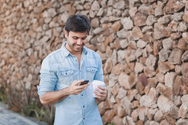 Retrato de jovem bebendo café na rua enquanto usa telefone celular — Fotografia de Stock