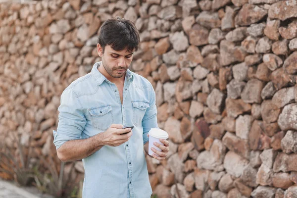 Porträtt av ung man dricka kaffe på gatan medan du använder mobiltelefon — Stockfoto