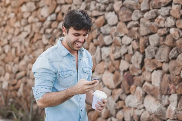 Retrato de jovem bebendo café na rua enquanto usa telefone celular — Fotografia de Stock