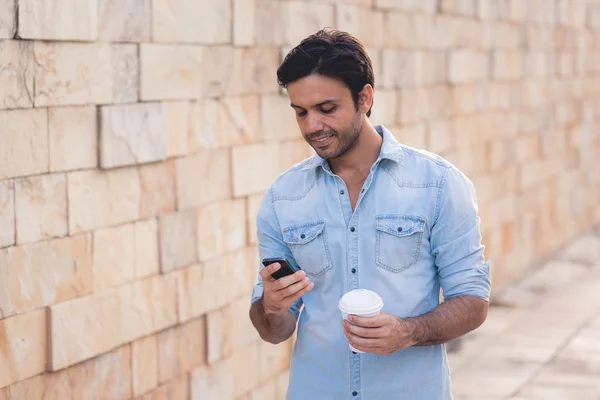 Portret młodzieńca, picie kawy na ulicy podczas korzystania z telefonu komórkowego — Zdjęcie stockowe