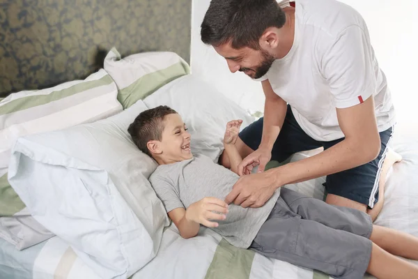 Ojciec łaskotanie syna na łóżku — Zdjęcie stockowe