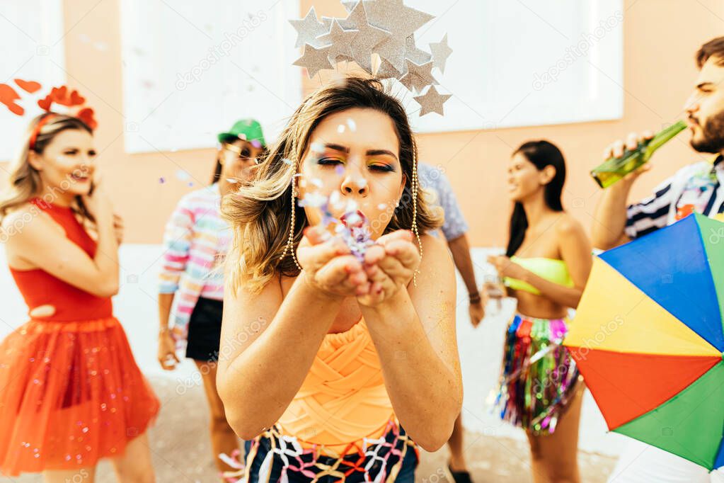 Brazilian Carnival. Young woman enjoying the carnival party blowing confetti