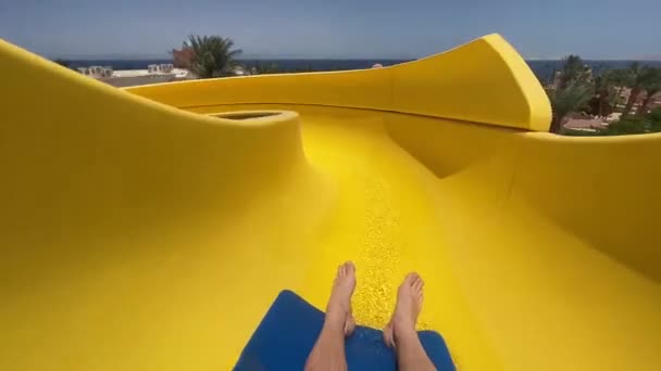 若い男は水公園の黄色の水のスライドに沿って速く移動します — ストック動画