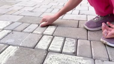 Çömelmiş bir kız kaldırım taşlarına tebeşirle çiziyor. Yakın çekim görünümü 