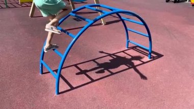 Kız merdivenlerden çocuk parkına çıkıyor. Kollar yanlara, dengeler ve dengeyi koruyor.. 