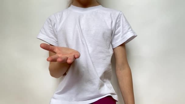 女の子は彼女の手を伸ばし 何かを与えるために彼女を尋ねます グレーの背景の前に白いTシャツの座席を着て若い女性のクローズアップビュー — ストック動画